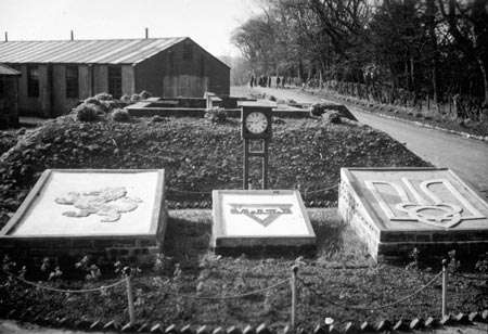 Decorative panels and planting beside a camp hut and road, with trees behind.