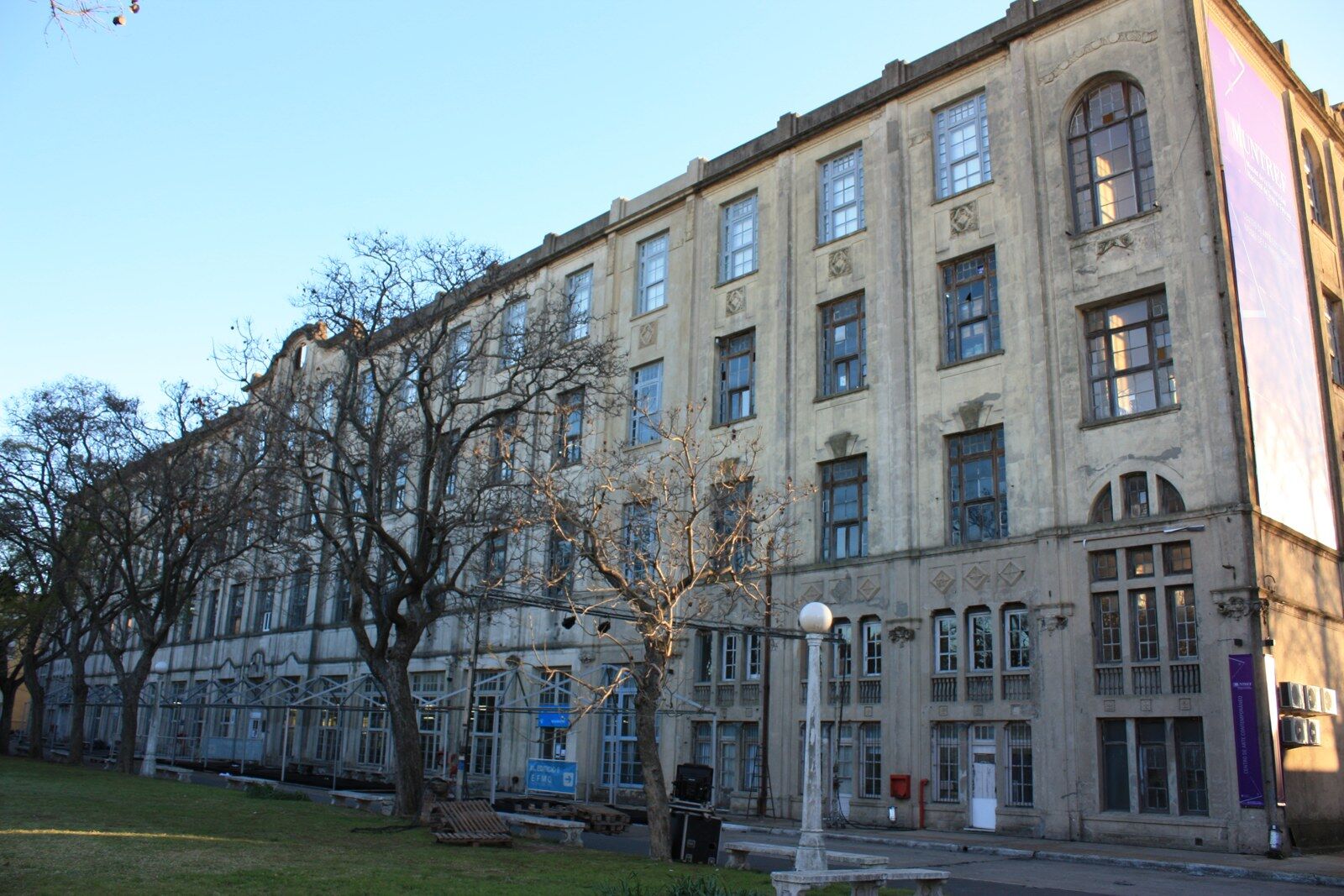 A long four-storey stone building with rows of tall windows, seen from a grassed area with bare trees in front of it.