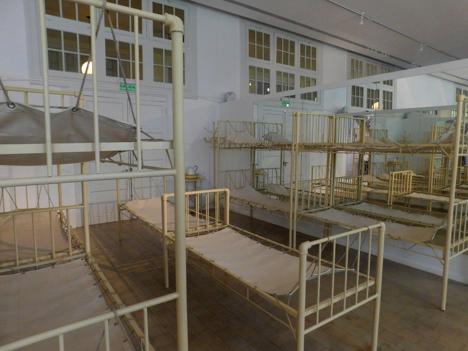 A museum room in the former Hotel de Inmigrantes lined with rows of cream-painted iron bunk beds with canvas mattresses.