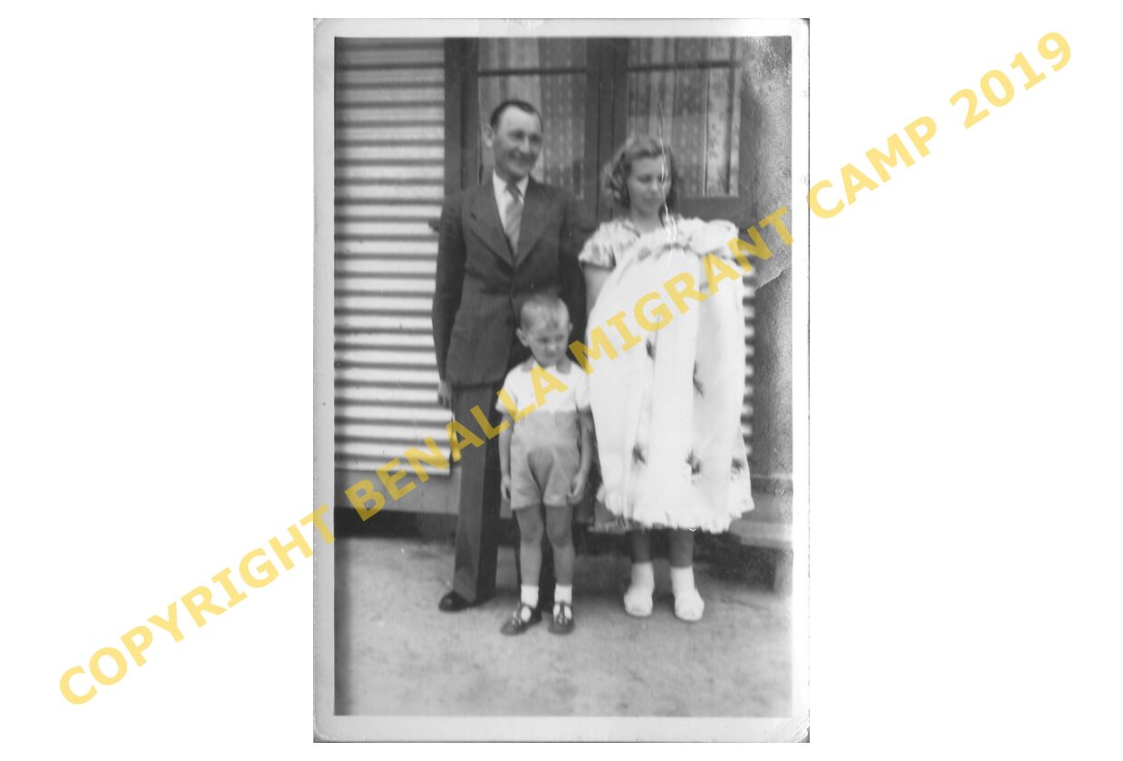 Two adults with a boy and a baby beside a corrugated building.