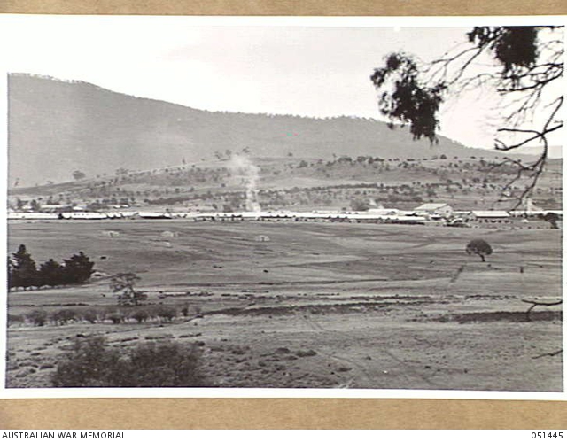 Rows of military camp buildings across open land beneath a hillside.