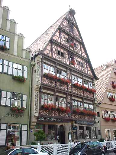 Tall timber-framed hotel front with a steep gable and window boxes of red flowers, seen from the street.