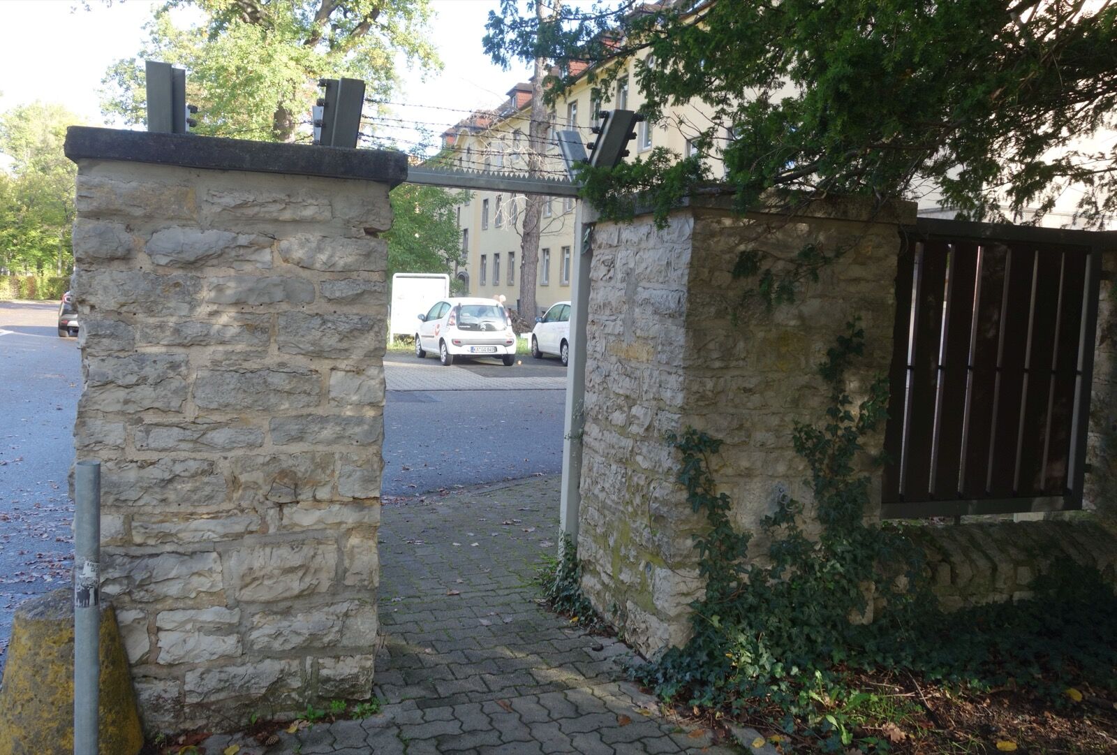 A surviving stretch of barracks boundary wall in Karlsruhe with a pedestrian gateway beside the site of the former vehicle barrier.