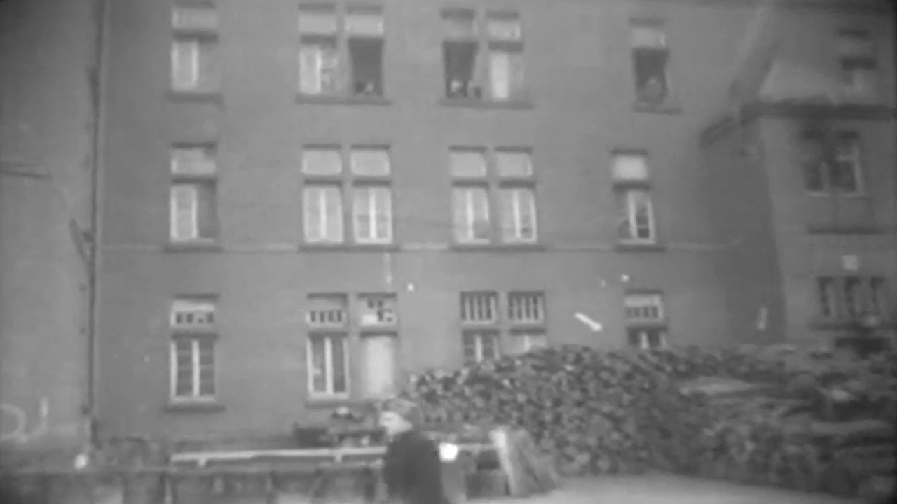 A four-storey barrack block with rows of windows and firewood stacked along its front.