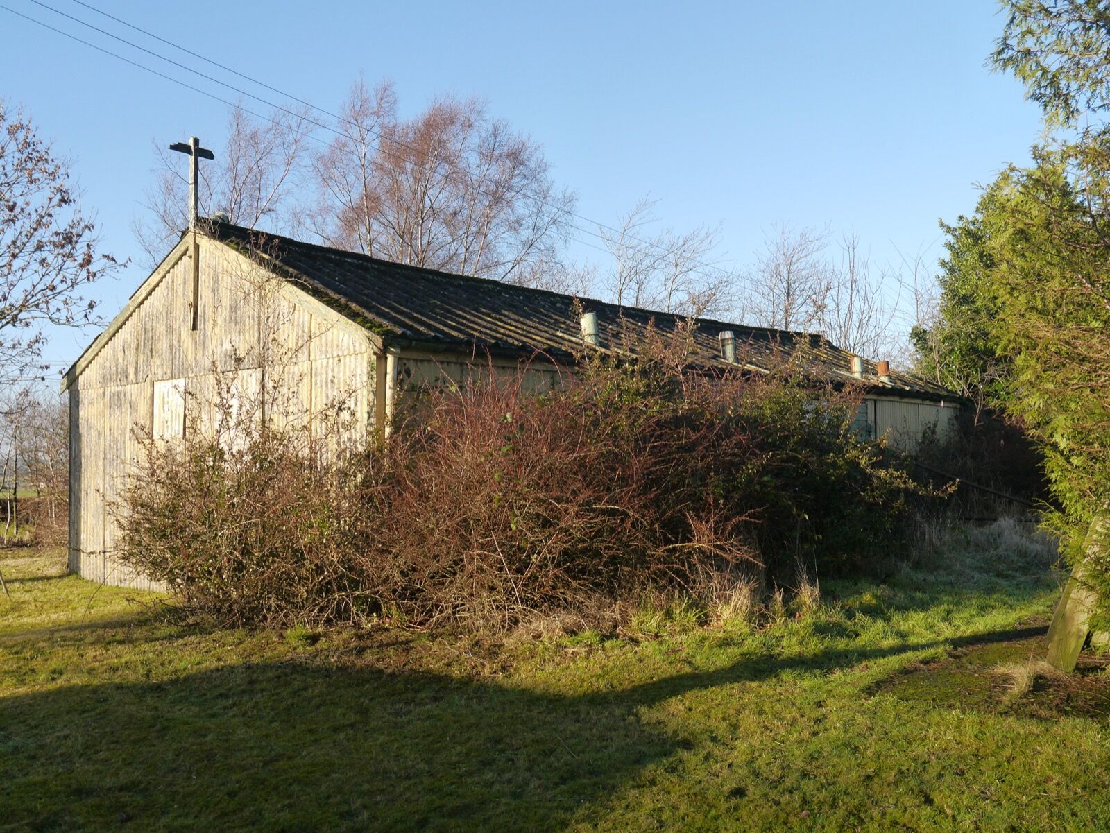 A long timber-clad hut with a corrugated roof at Hallmuir, a plain cross on its gable.
