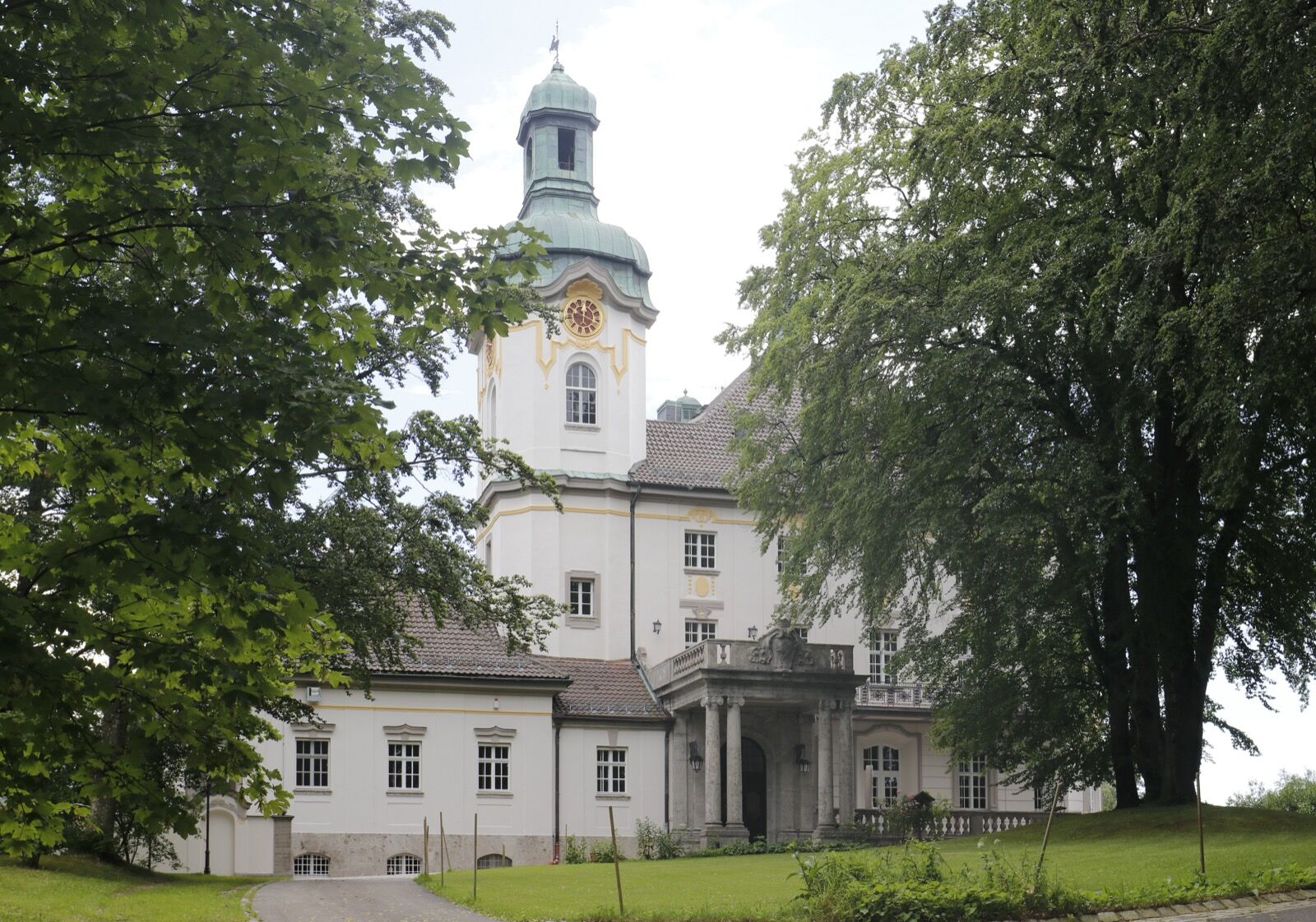Schloss Hirschberg am Haarsee, a long white country house with a steep roof and corner tower, standing among trees.