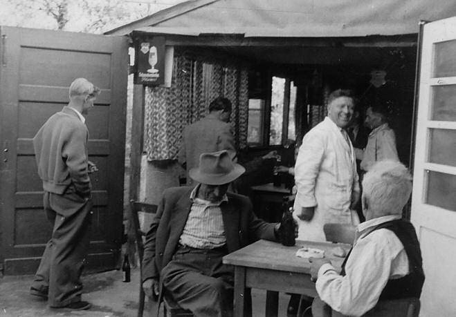 The entrance to one of the camp canteens at Lintorf, with people standing and sitting outside.