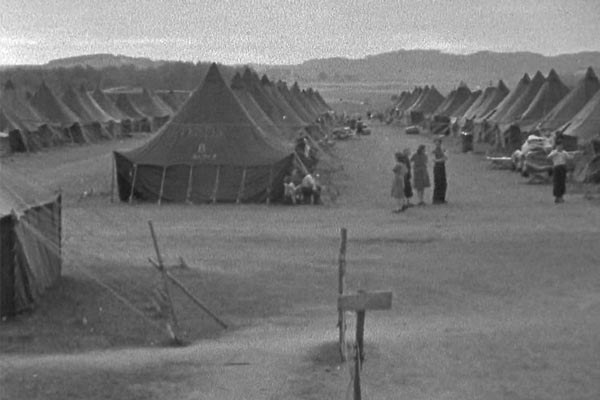 Black-and-white photograph of long rows of ridge tents pitched on open ground at the edge of a settlement.
