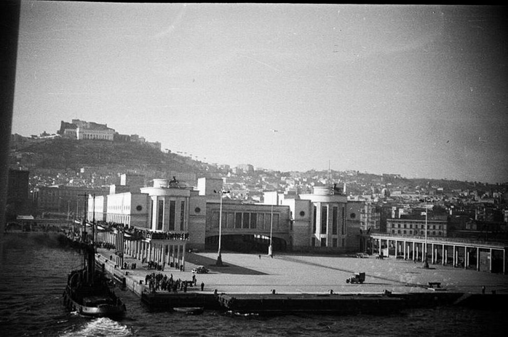 The Stazione Marittima at Naples seen from the water, with its quay, forecourt and the city rising behind.