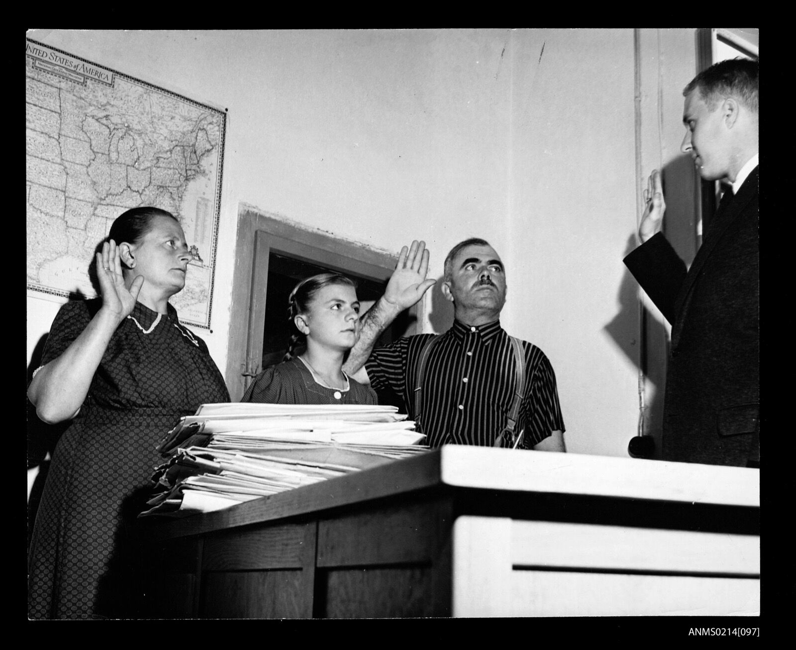 A man, woman and child standing with raised right hands before an official at a desk in an office.