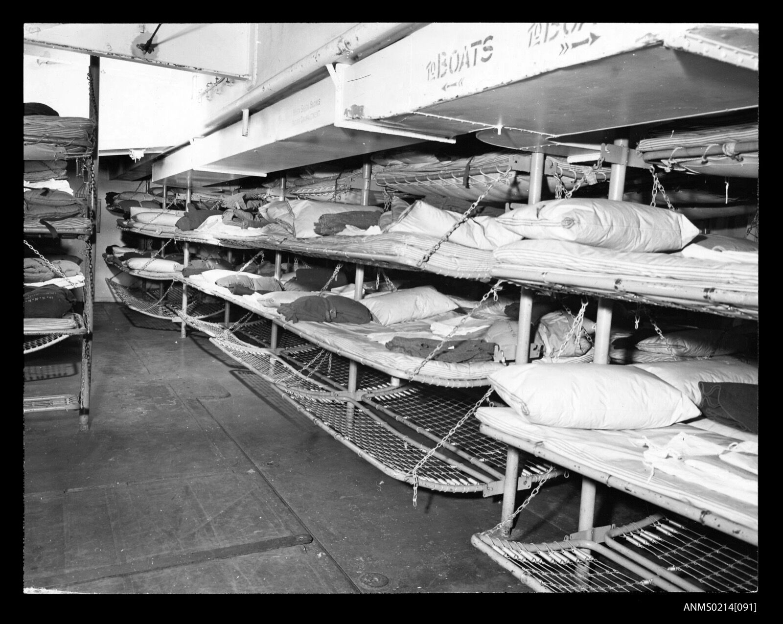 Rows of tiered canvas berths made up with blankets in the hold of a troop transport.