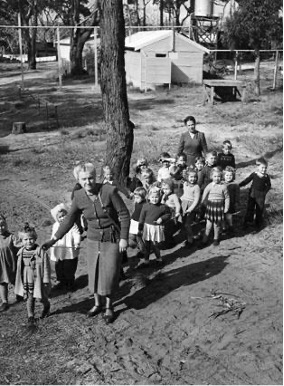 Kindergarten children walking in the grounds of the Nelson Bay hostel holding a guide rope, 1951.
