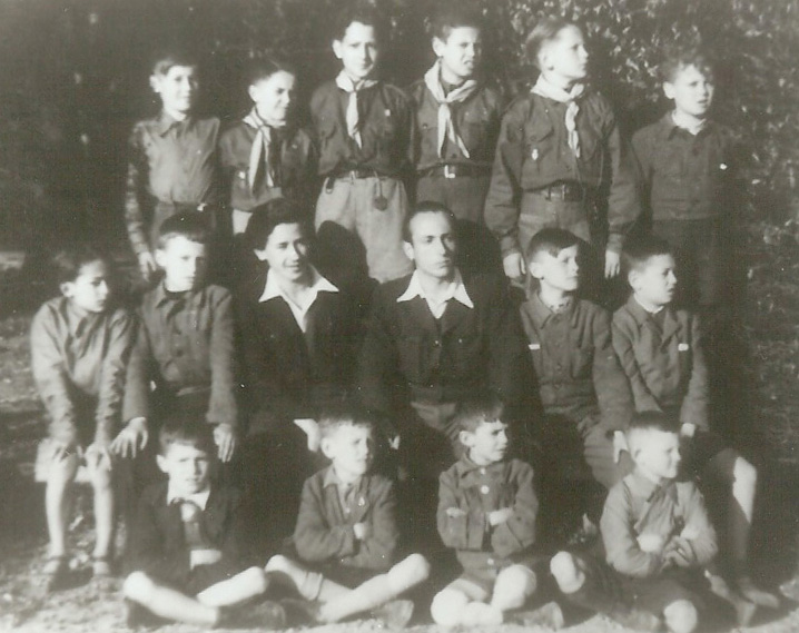 Sepia group photograph of about eighteen boys in scout neckerchiefs arranged in three rows on grass.