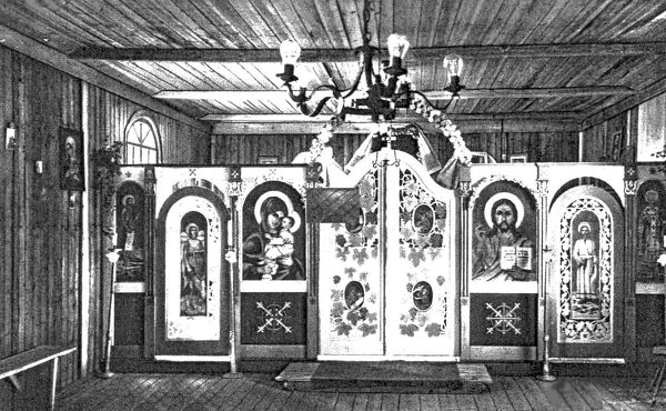 A five-panel painted iconostasis across a boarded wooden hut interior, with a chandelier above