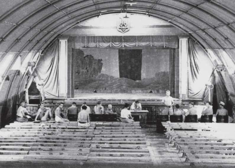 Interior of the Rimini camp theatre, with numbered benches and a stage.