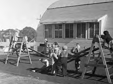 Children using playground equipment beside camp buildings.