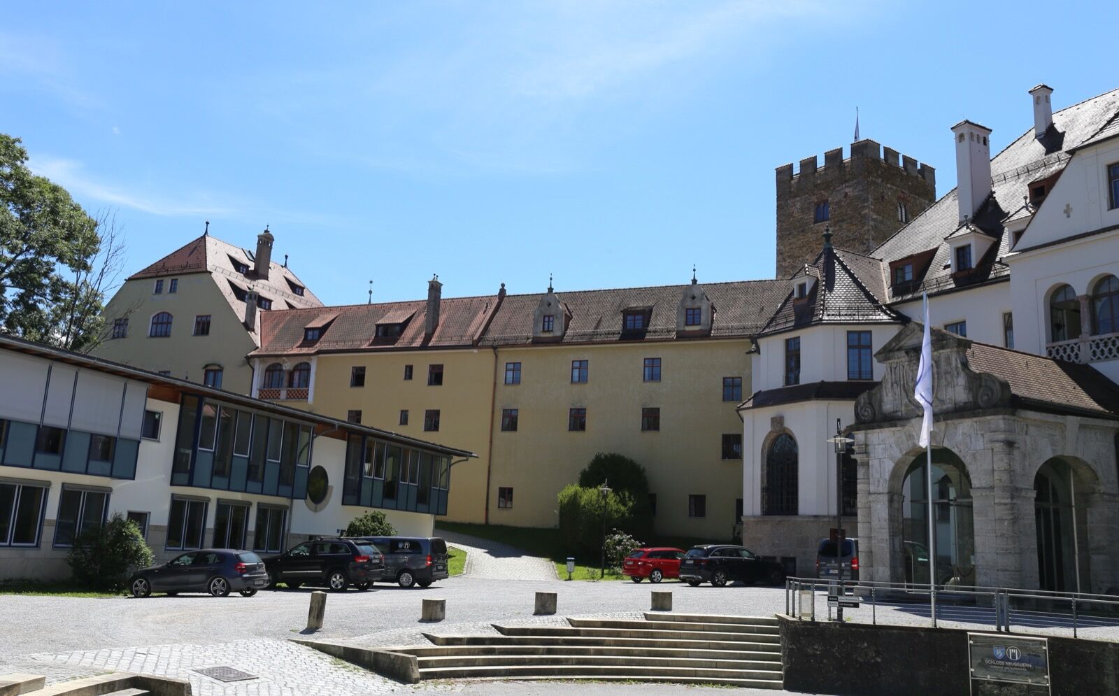 Schloss Neubeuern seen from below, its rendered ranges and onion-domed corner tower rising from a wooded outcrop above the town.