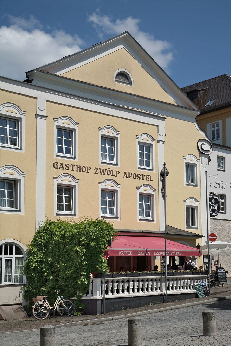 A tall cream-painted inn with a pedimented gable, its name lettered in dark capitals across the first floor above a red awning.